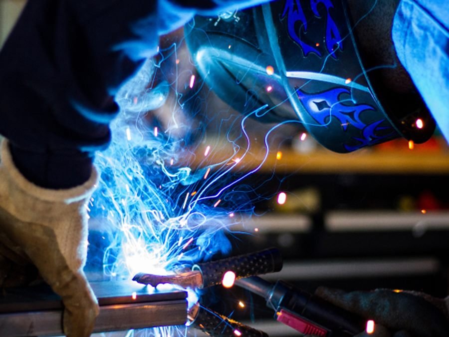 Welder in helmet and gloves welding steel, with sparks flying