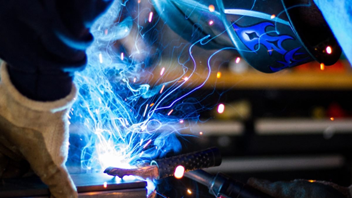 Welder in helmet and gloves welding steel, with sparks flying