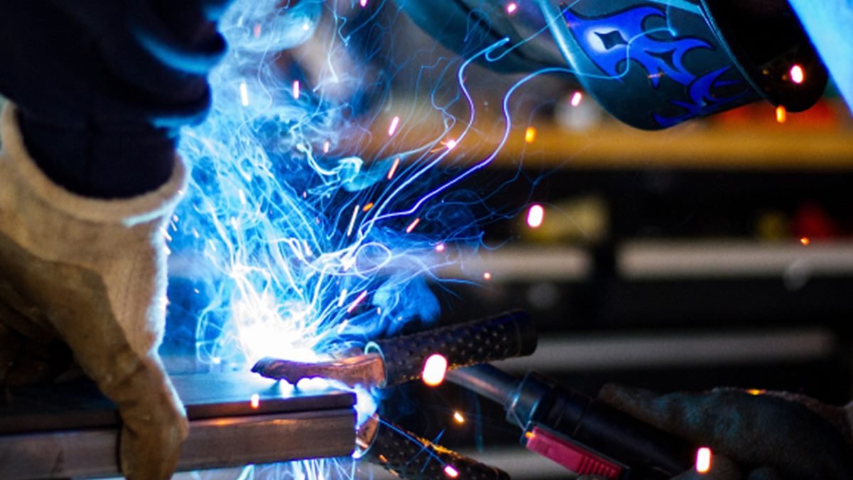 Welder in helmet and gloves welding steel, with sparks flying